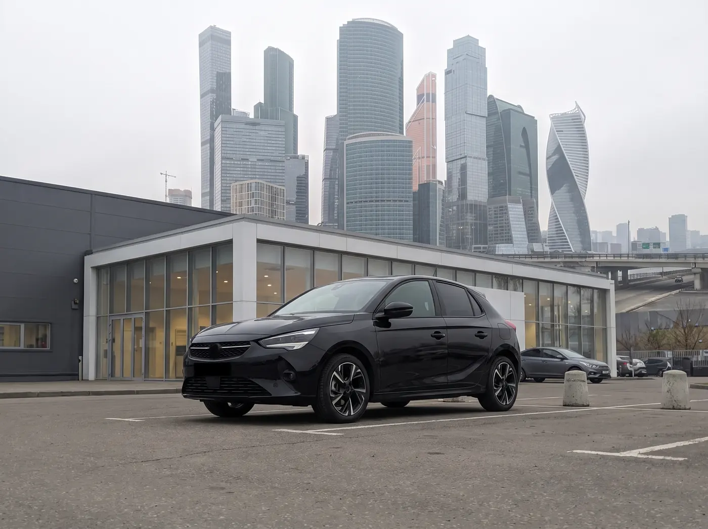 A black hatchback on the dealership forecourt, skyline behind, photographed on a grey day